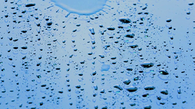 阳光下的雨点或水滴在玻璃上流动。特写雨落溅在明亮的表面的镜子的汽车背景视频素材