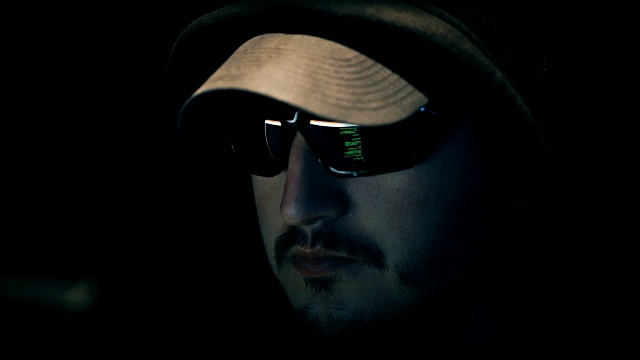 一名男性黑客正在电脑上工作，绿色代码字符反映出他的玻璃视频素材