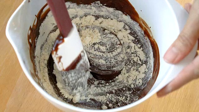 用手把融化的巧克力奶油和面粉混合在白色的碗里。视频素材