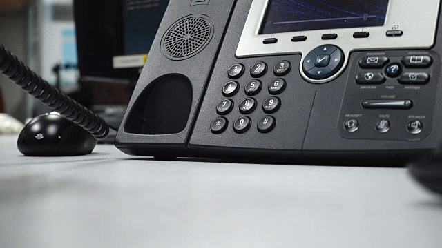 手拿起黑色的电话，拨了一个号码，然后挂了起来，背景是一间办公室的电脑室。景深浅。视频素材