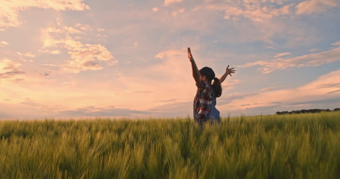 无忧无虑，精力充沛的年轻少女农民与双臂伸开在绿色的麦田，慢动作视频下载