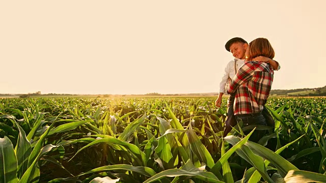 女农民和儿子站在阳光明媚、田园诗般的农村玉米地里，实时拍摄视频素材