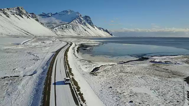 在冰岛东海岸的冬季，飞过冰雪覆盖的道路和雪山景观视频素材