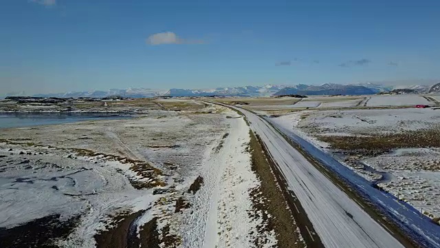 在冰岛东海岸的冬季，飞过冰雪覆盖的道路和雪山景观视频素材