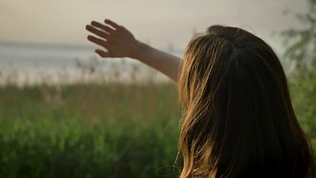 年轻快乐的快乐女孩站在海边，用双手合上阳光，令人目眩，阳光剪影50帧视频素材