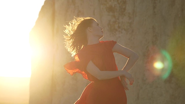 身着红裙的女孩在阳光和悬崖的背景下摆姿势视频素材
