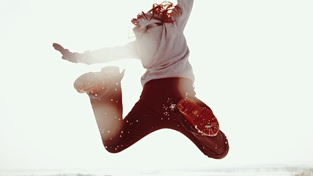 精力充沛的女人跳跃着，踢起雪花撞击阳光灿烂的天空，超慢的动作视频下载