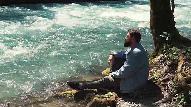 一个英俊的男人独自躺在森林的河岸上视频素材