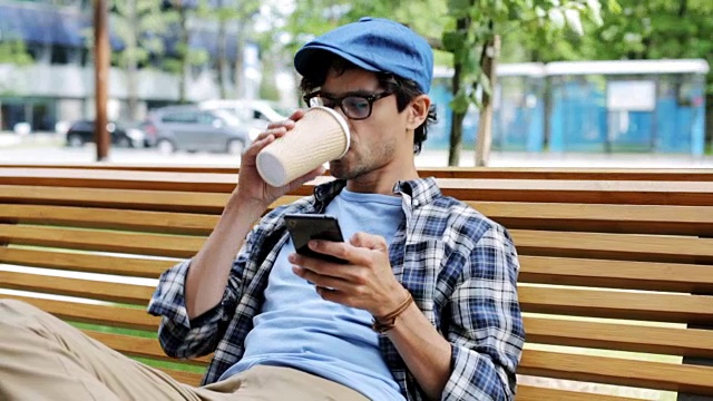 男人拿着智能手机在城市街道的长椅上喝咖啡视频素材