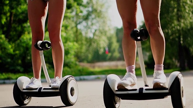 美丽的匀称的腿，年轻的女孩在短chertah近距离白色陀螺仪电动赛格威骑通过公园视频下载