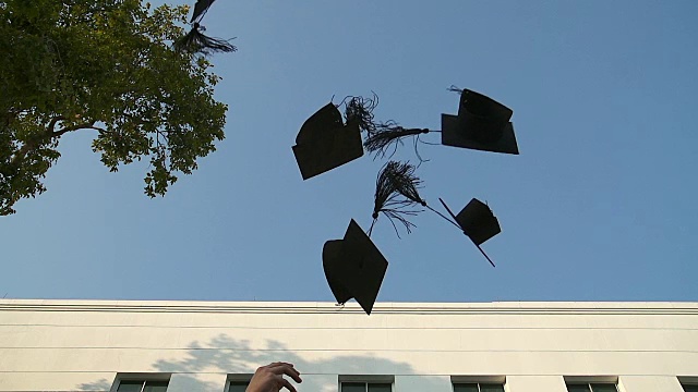 快乐的学生们穿着长袍，把学位帽抛向空中。教育、毕业与人理念-视频下载