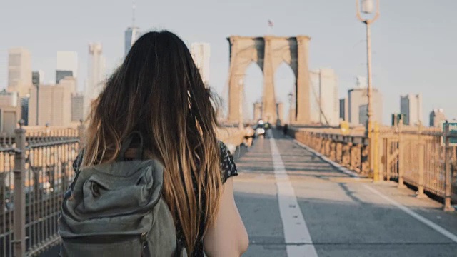 镜头跟随一个背着背包的年轻女子沿着布鲁克林大桥走，在一个美丽的阳光灿烂的夏天4K视频素材