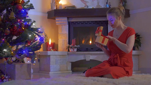 年轻的女性坐在仙女地毯上，打开她的礼物靠近圣诞树视频下载