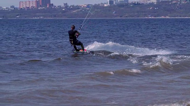 慢镜头:一名男子的风筝滑板沿着一条大河的波浪优美地滑行。水花四溅向不同的方向。阳光明媚的春天。视频下载