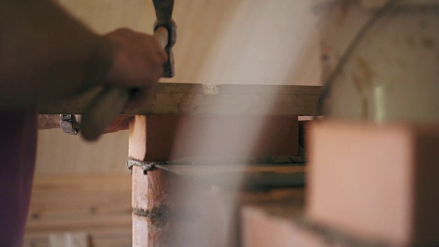 建筑工正在用锤子敲打一块红砖，然后把它弄平。一个建筑工人正在建一个砖砌壁炉视频素材