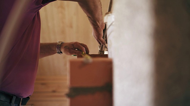 一名建筑工人正在用锤子对准壁炉的砖面。一个男人正在用轮盘赌来测量红砖之间的距离视频素材