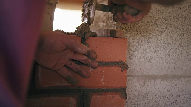 泥瓦匠在壁炉的红砖之间用水泥和抹刀的溶液填充视频素材