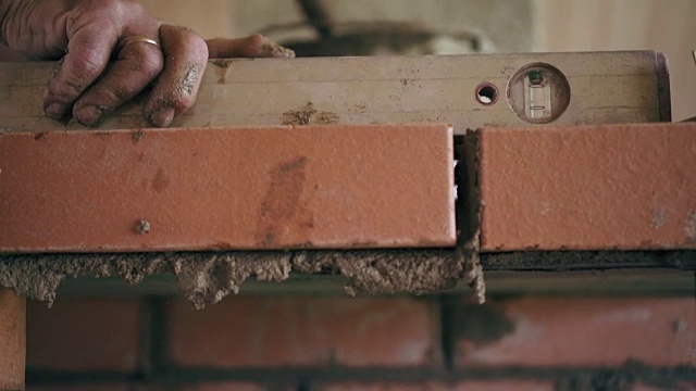一个建筑工人正在把一块砖放在一层水泥溶液上建一个壁炉。砖墙的特写镜头视频素材