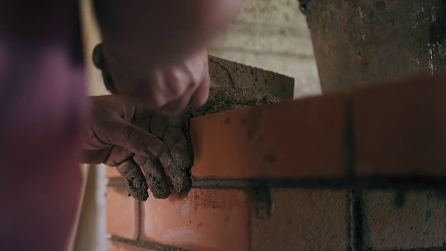一位专业建筑工人正在用红砖和水泥溶液建造一堵砖墙。一个男人的特写镜头对准了工地上砖块的水平视频素材