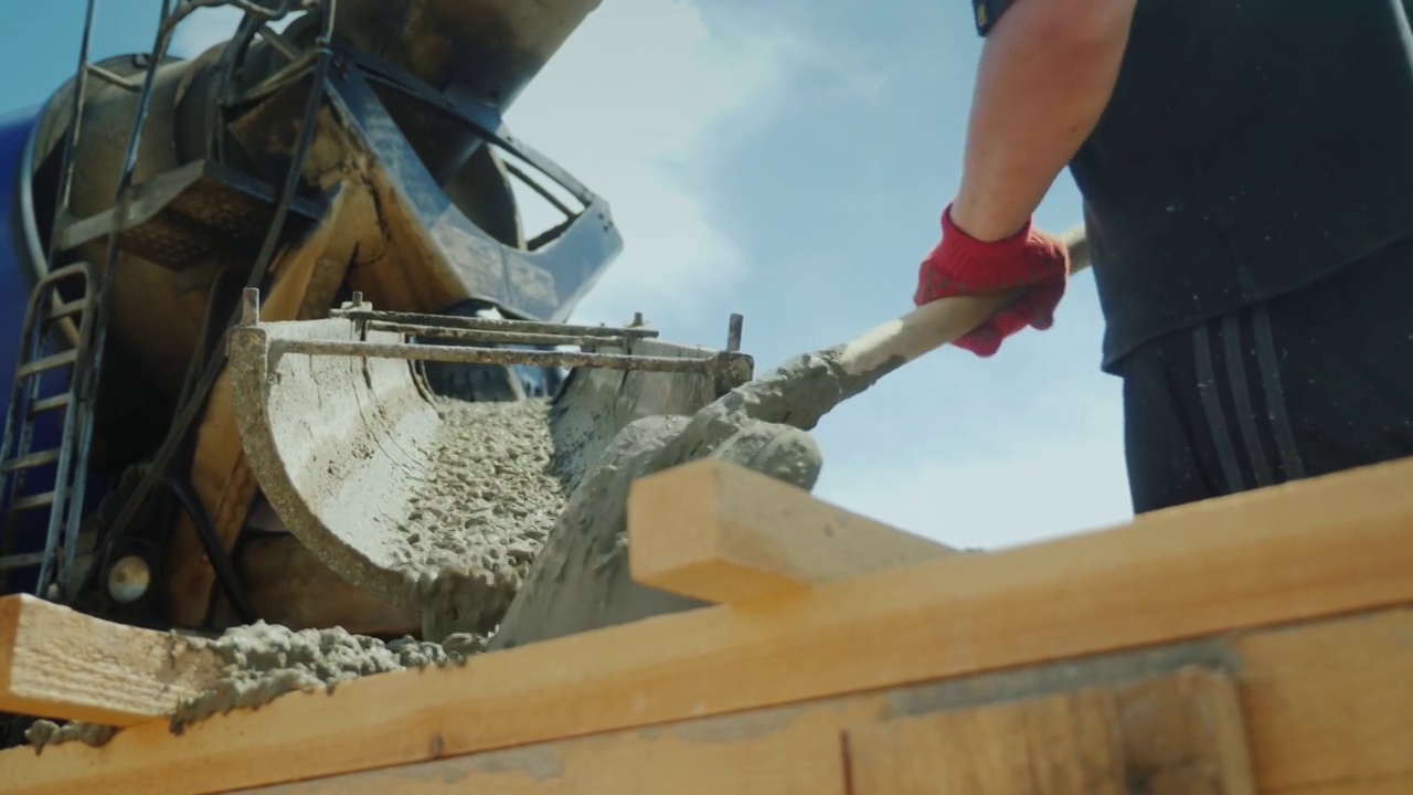 工人从工业搅拌机中取出混凝土，就像铲子一样工作。建筑工地繁重的体力劳动。低角度拍摄视频素材