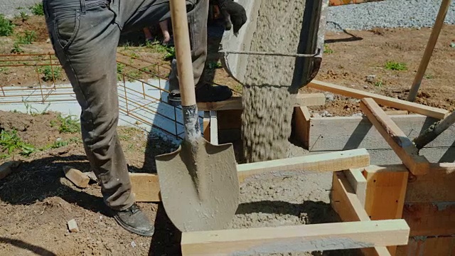 将混凝土浇入木模中。旁边是一个拿着铁锹的工人。建设别墅视频素材