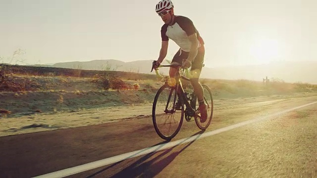 慢动作年轻男子在沙漠道路上骑自行车在日落与镜头光晕视频素材
