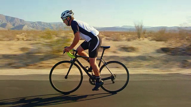 年轻的健康男子在沙漠道路上骑自行车在日落视频下载