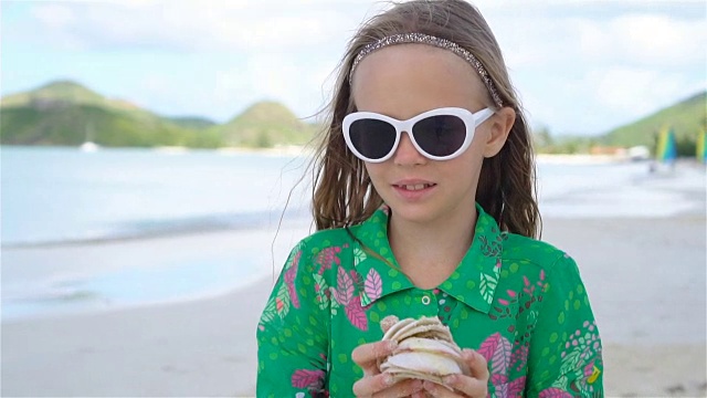 热带海滩上，一个手里拿着贝壳的可爱小女孩视频素材