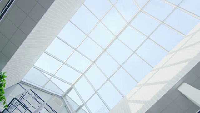 医院/大楼/商场/超市的玻璃天花板的低角度旋转拍摄。高大的白色建筑，阳光从窗户射出来。视频下载