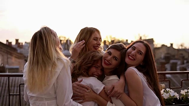 迷人的白人女孩站在外面的阳台上拥抱。六个漂亮的年轻女人穿着白衬衫，涂着红色的口红。母鸡派对。晚上黄昏。爱和友谊视频素材
