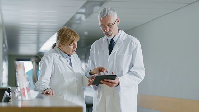 在医院，两位医生站在前台，用平板电脑聊天，分享信息。拥有病人和医务人员的现代化医院。视频素材