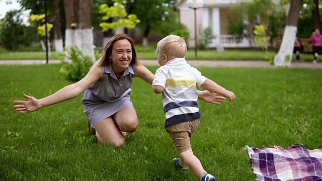 金发小男孩跑向他的妈妈。妈妈张开双手，微笑着抱住了宝宝。快乐的母亲，慈爱的儿子。在户外野餐。绿色公园。慢动作视频素材
