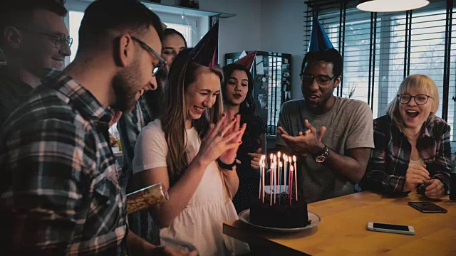 快乐的白人女孩在生日蛋糕上用蜡烛许愿。多民族朋友在惊喜派对慢镜头视频素材