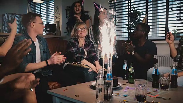 多民族的朋友在惊喜派对上用闪亮的烟花蛋糕祝贺害羞的白种人生日女孩视频素材