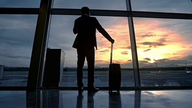 日落时分，一个商人走到机场的玻璃墙前打电话视频素材