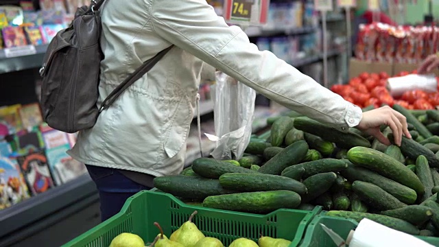 一位年轻女子在超市挑选和购买新鲜黄瓜。视频素材