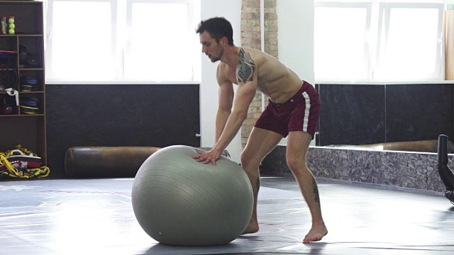 体格健壮的年轻人在健身球上滚动，练习平衡视频下载