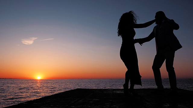 年轻的西班牙夫妇的剪影在夕阳下的大海背景。男人和女人跳舞拉丁美洲的感官舞蹈:bachata, salsa或kizomba。慢动作视频素材