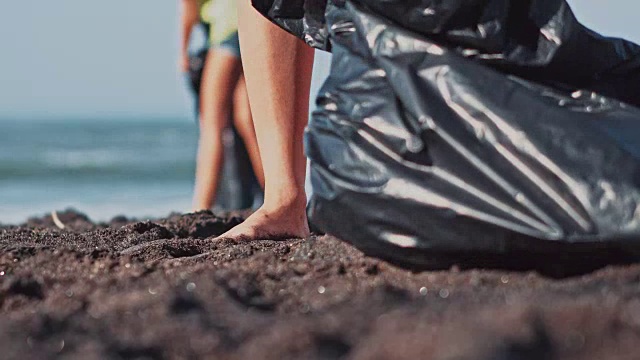 一群志愿者正在清理海滩。志愿者举起一个塑料瓶扔进袋子里。志愿服务和回收概念。环保意识概念拷贝空间视频素材