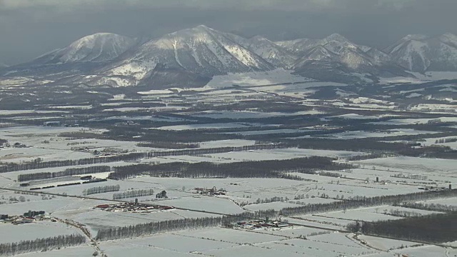在雪原和山脚下的城镇上空的空中轨道。日本。视频下载