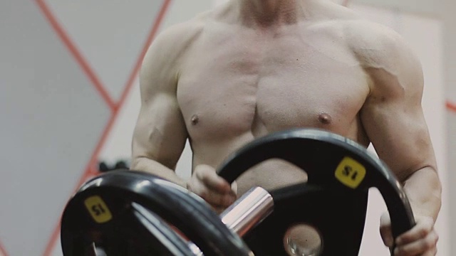 过渡镜头，坚定的肌肉男子把沉重的盘子上的杠铃和举重在健身房视频下载