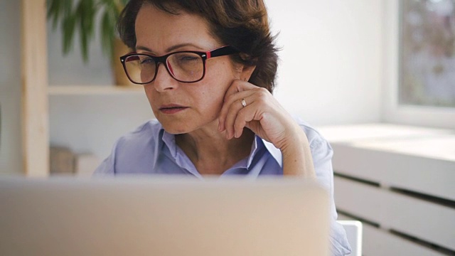 一位年长的商务女士坐在家里的笔记本电脑屏幕前的肖像视频下载