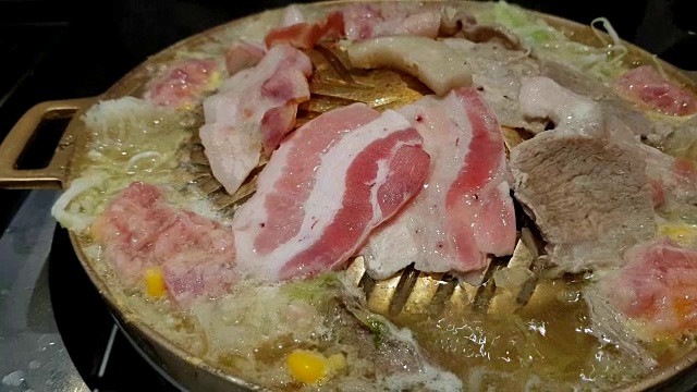 在黄铜锅上烤猪肉片和烤肉。锅的一边有开水煮蔬菜。视频素材