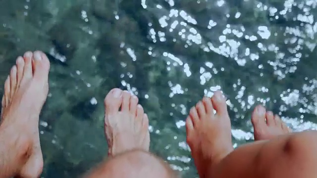 一对夫妇坐在码头上，摇摆着脚在涟漪的海水上视频下载