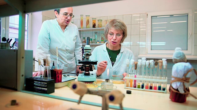 两位50多岁的女性科学家，在大学微生物实验室与显微镜和细菌培养一起工作视频下载