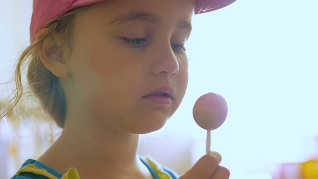 小女孩一边盯着镜头一边享受棒棒糖。孩子吃糖果，糖果，糖视频下载