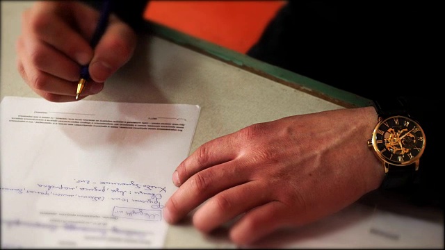 一个手里拿着钟的人在写信。男人的手的特写镜头。视频素材