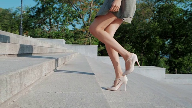 性感的腿和米黄色的高跟鞋爬上城市的楼梯。女商人独自走在大道上。夏天穿着短裙的漂亮女孩。慢动作视频素材