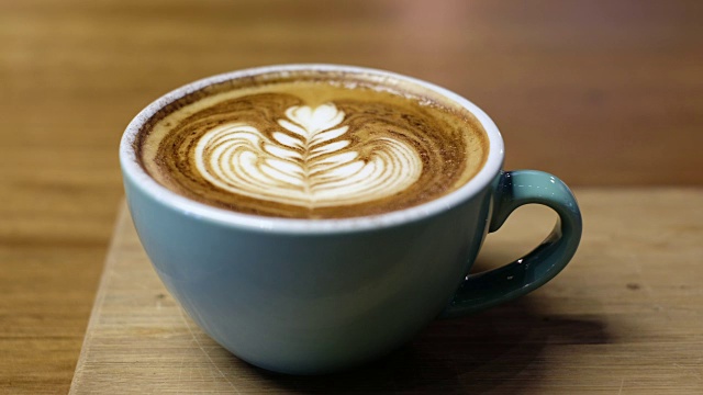 靠近热卡布奇诺咖啡杯拿铁艺术在木桌上，举起来喝在咖啡店视频下载