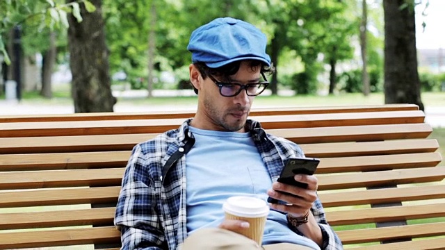 一个拿着智能手机在城市街道上喝咖啡的男人视频素材